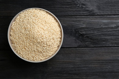 Photo of Sesame seeds in bowl on black wooden table, top view. Space for text