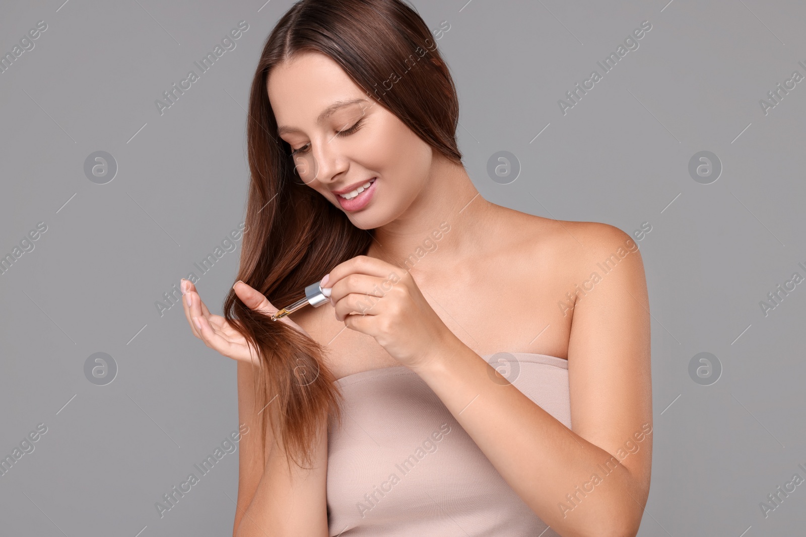 Photo of Beautiful woman applying serum onto hair on grey background