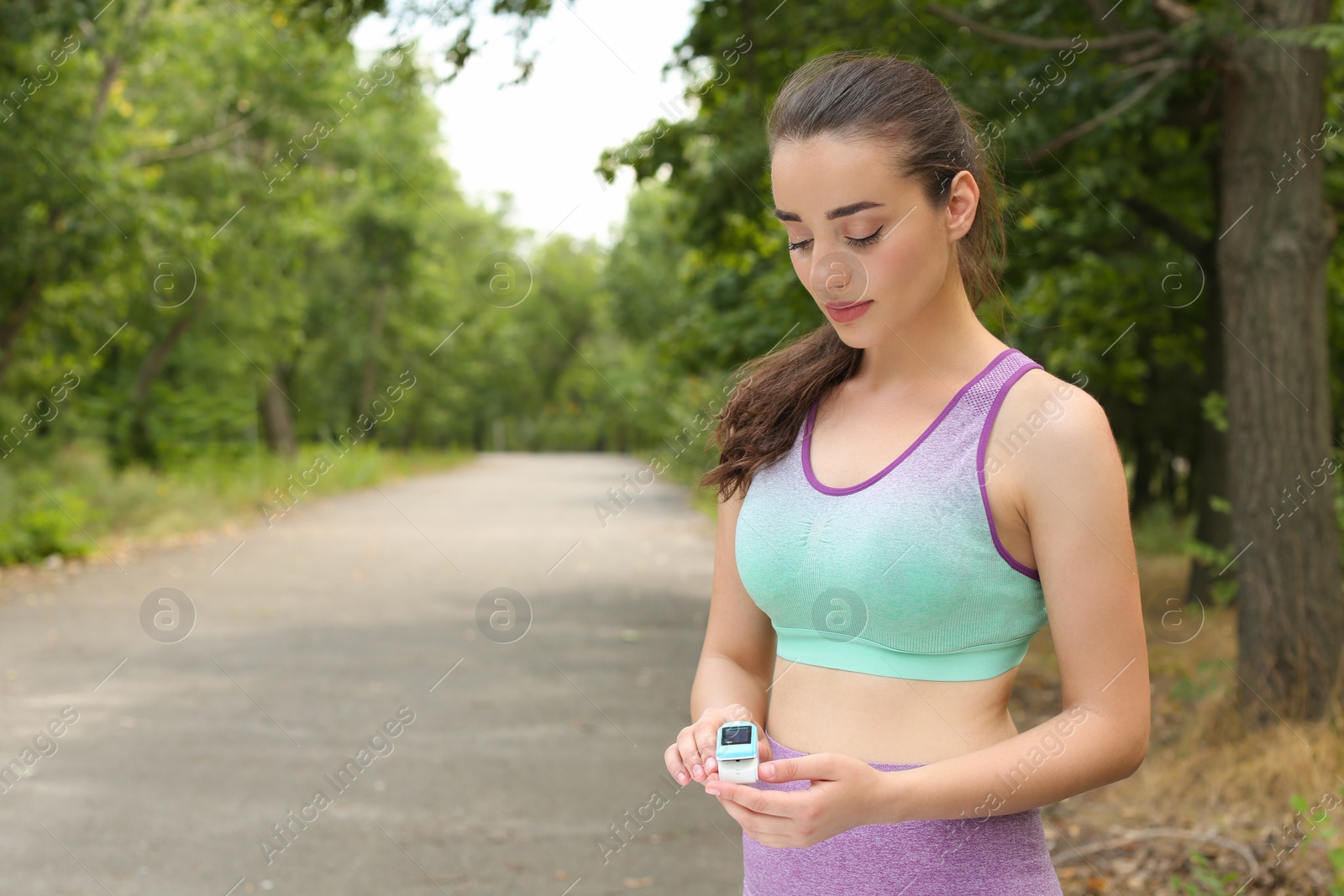 Photo of Young woman checking pulse with medical device after training in park. Space for text