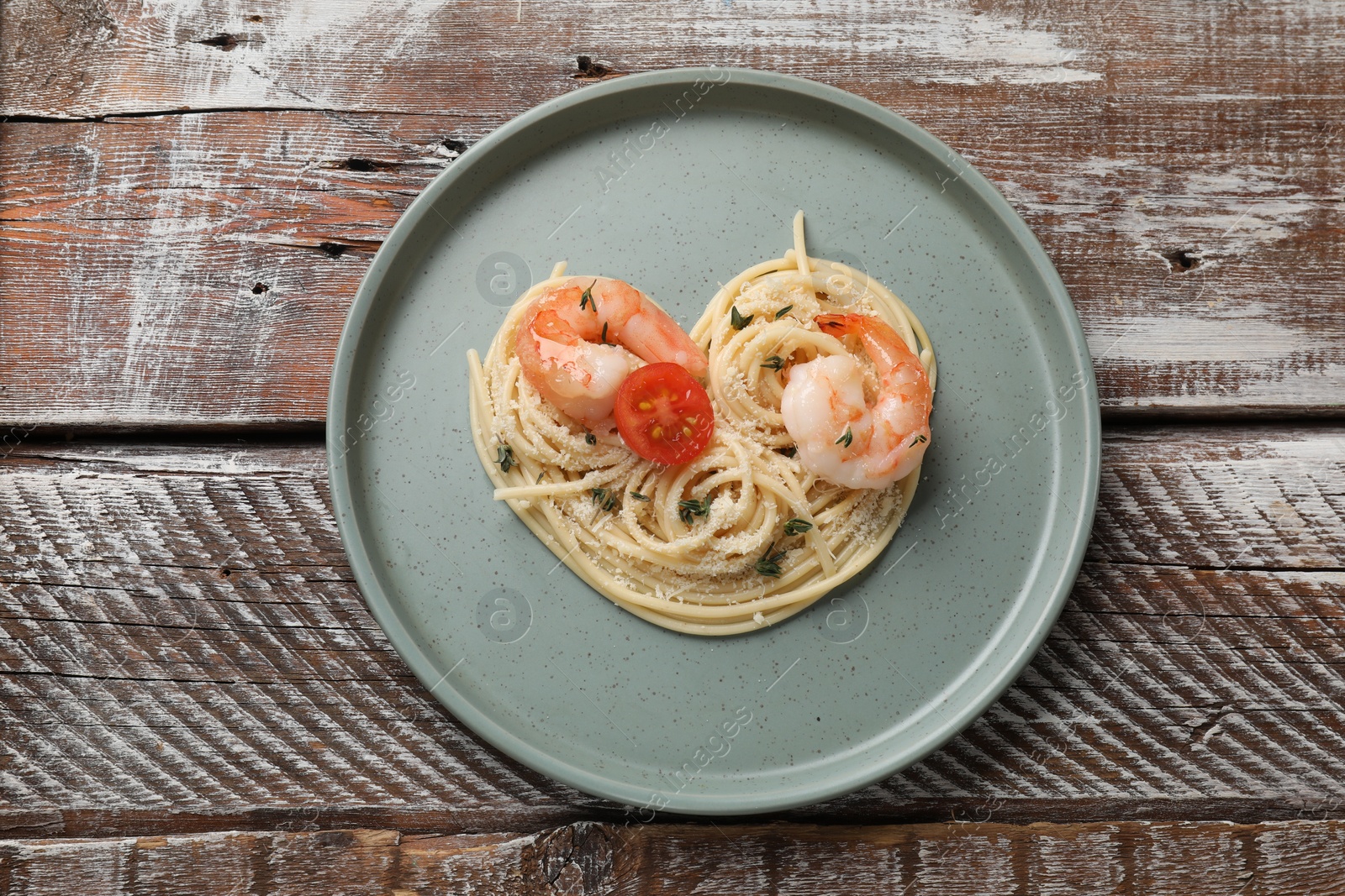 Photo of Heart made of tasty spaghetti, tomato, shrimps and cheese on wooden table, top view