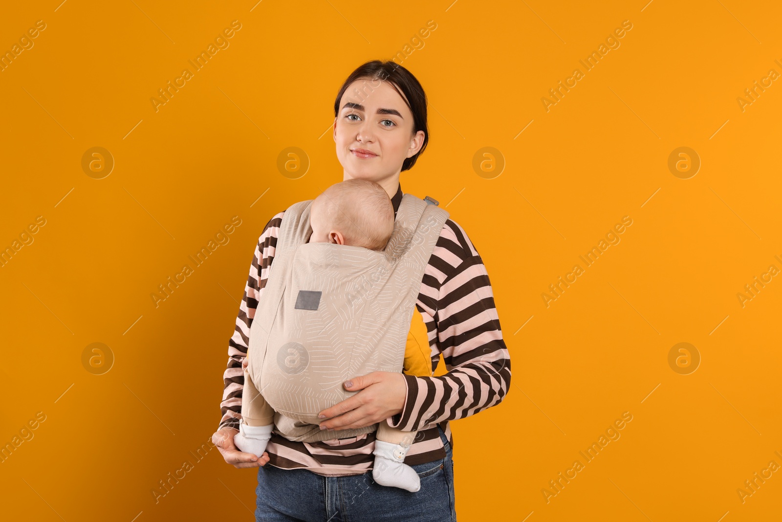 Photo of Mother holding her child in sling (baby carrier) on orange background