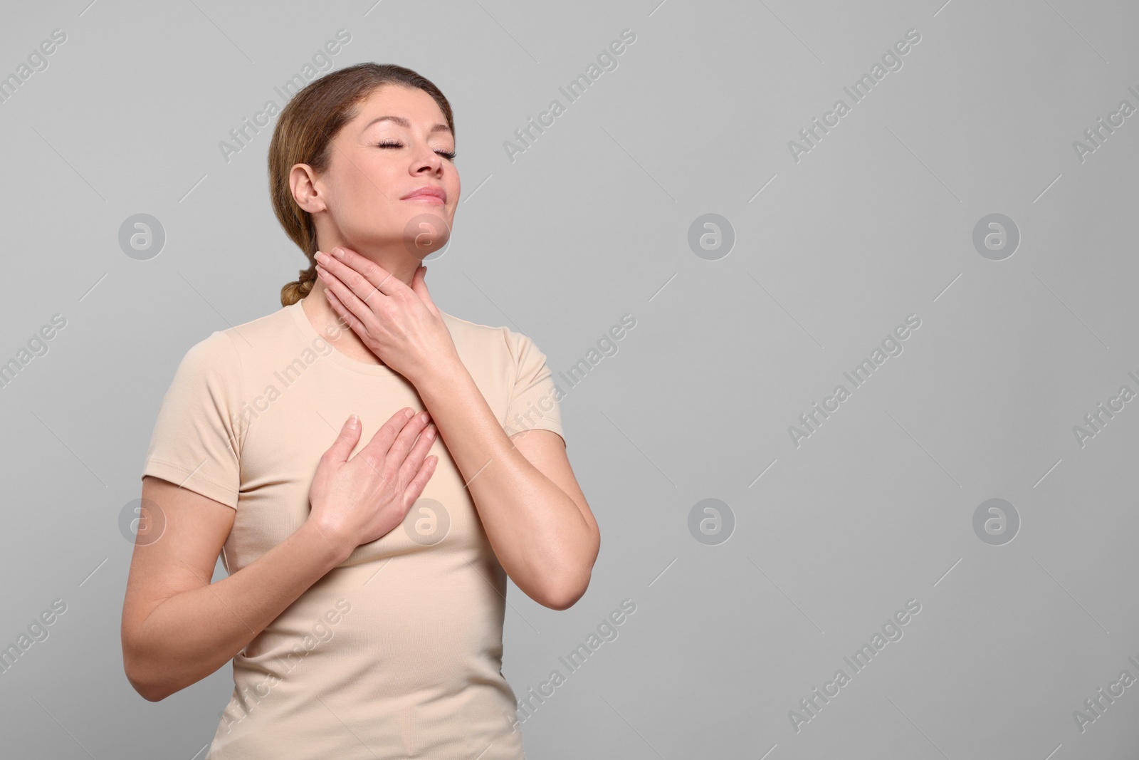 Photo of Woman suffering from sore throat on light grey background. Space for text