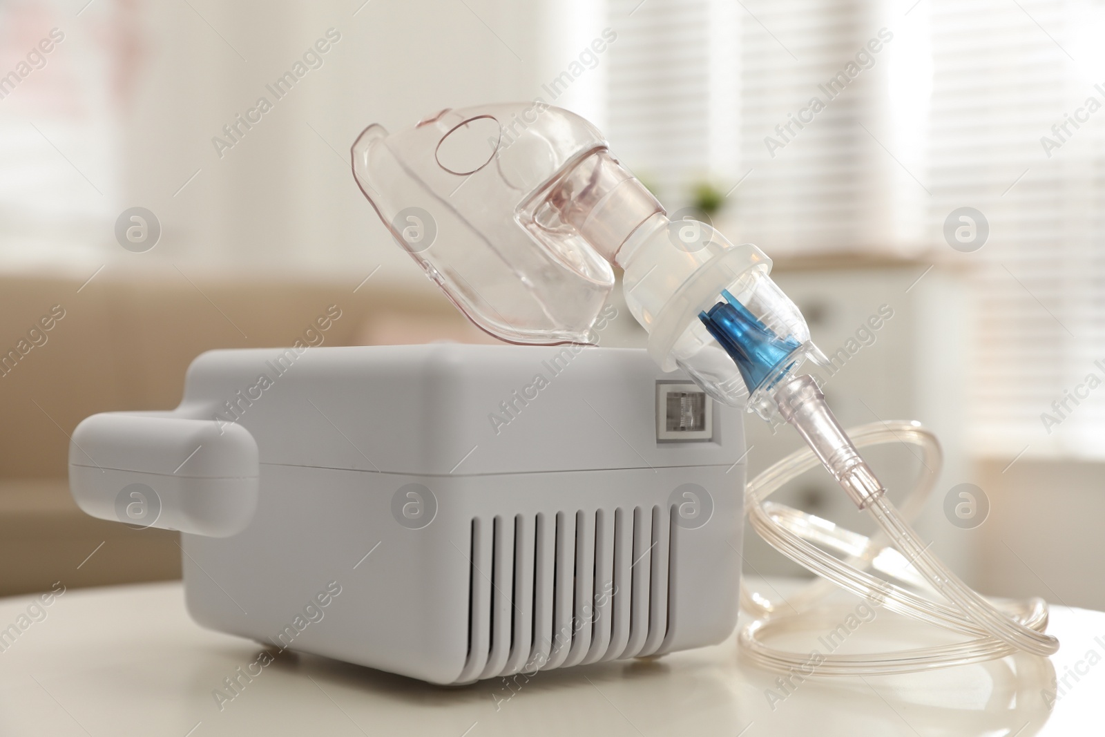 Photo of Modern nebulizer with face mask on white table indoors. Inhalation equipment