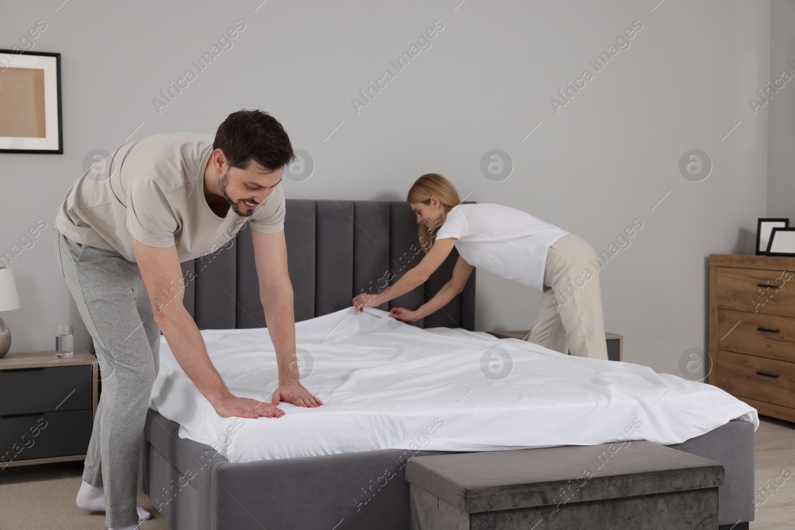 Photo of Couple changing bed linens in room. Domestic chores