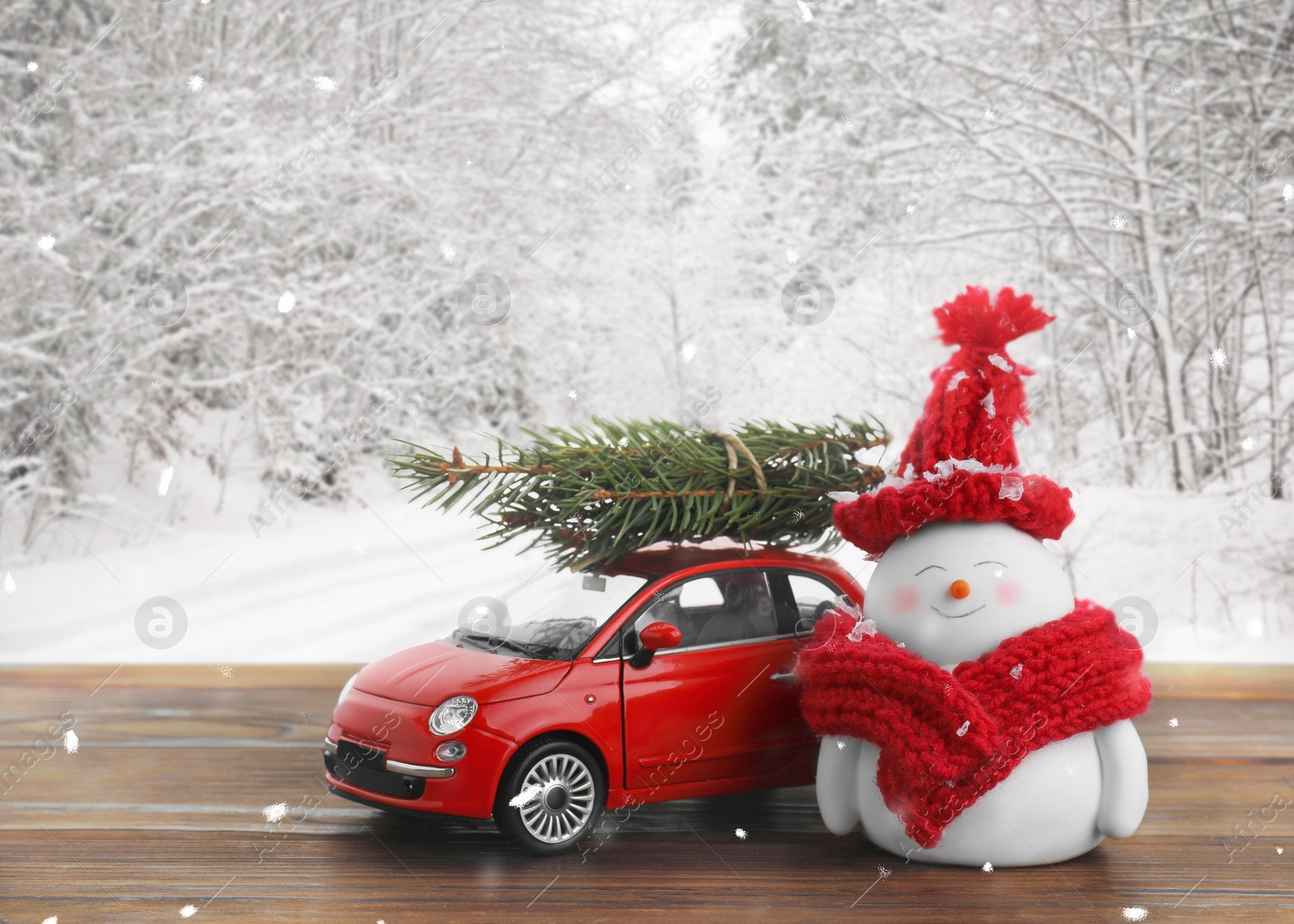 Image of Cute decorative snowman, toy car and fir tree branches on wooden table in snowy forest