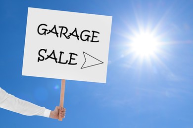 Woman holding sign with text GARAGE SALE against blue sky