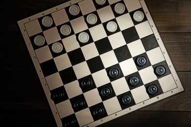 Photo of Checkerboard with game pieces on wooden table, top view