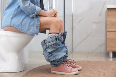 Photo of Woman suffering from hemorrhoid on toilet bowl in rest room, closeup