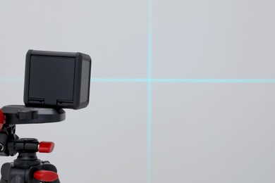 Photo of Cross line laser level on tripod in front of grey wall