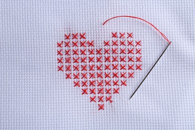 Photo of Embroidered red heart and needle on white cloth, top view