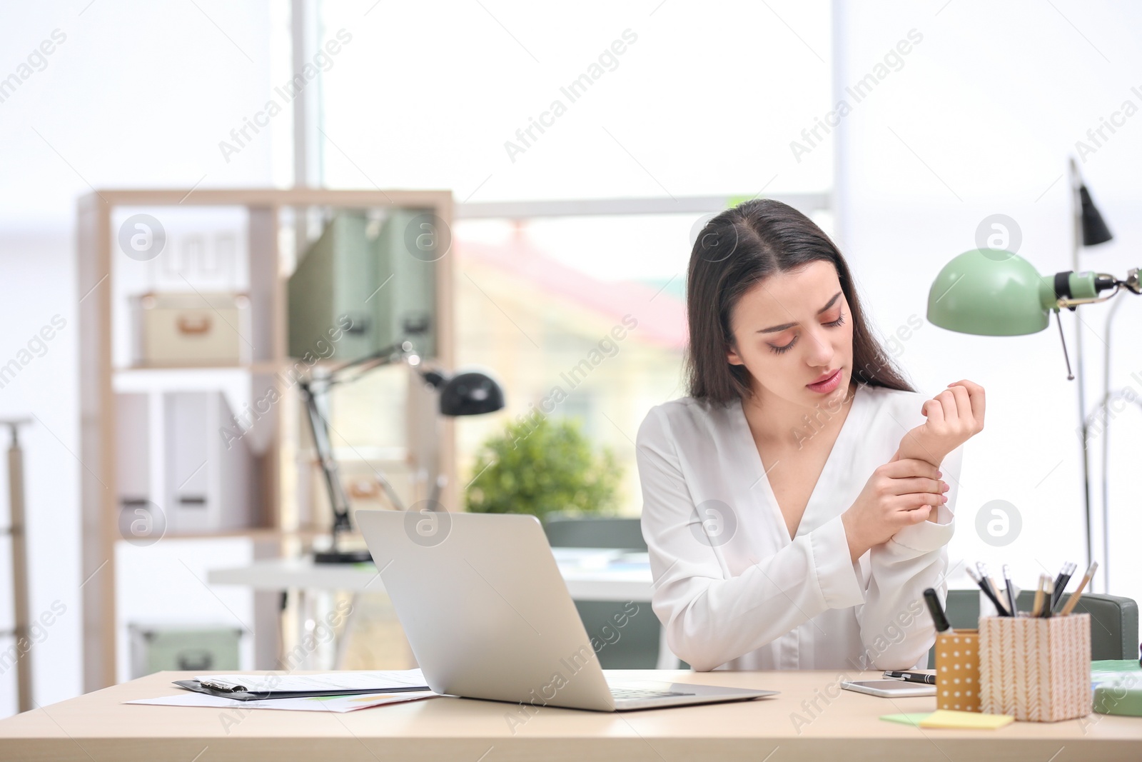 Photo of Young woman suffering from wrist pain in office