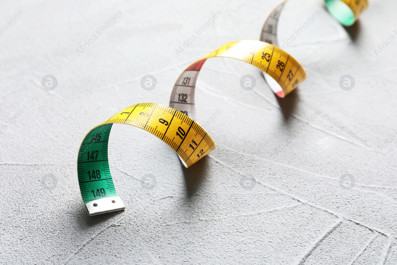 Photo of Measuring tape on grey background, closeup. Tailoring equipment