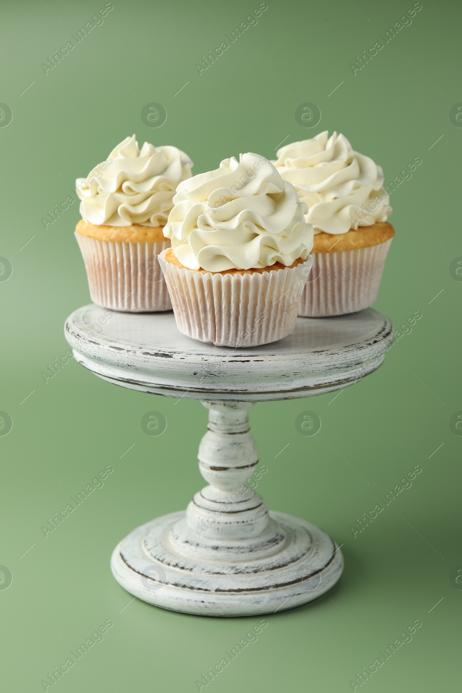 Photo of Tasty vanilla cupcakes with cream on green background