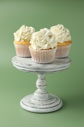 Tasty vanilla cupcakes with cream on green background