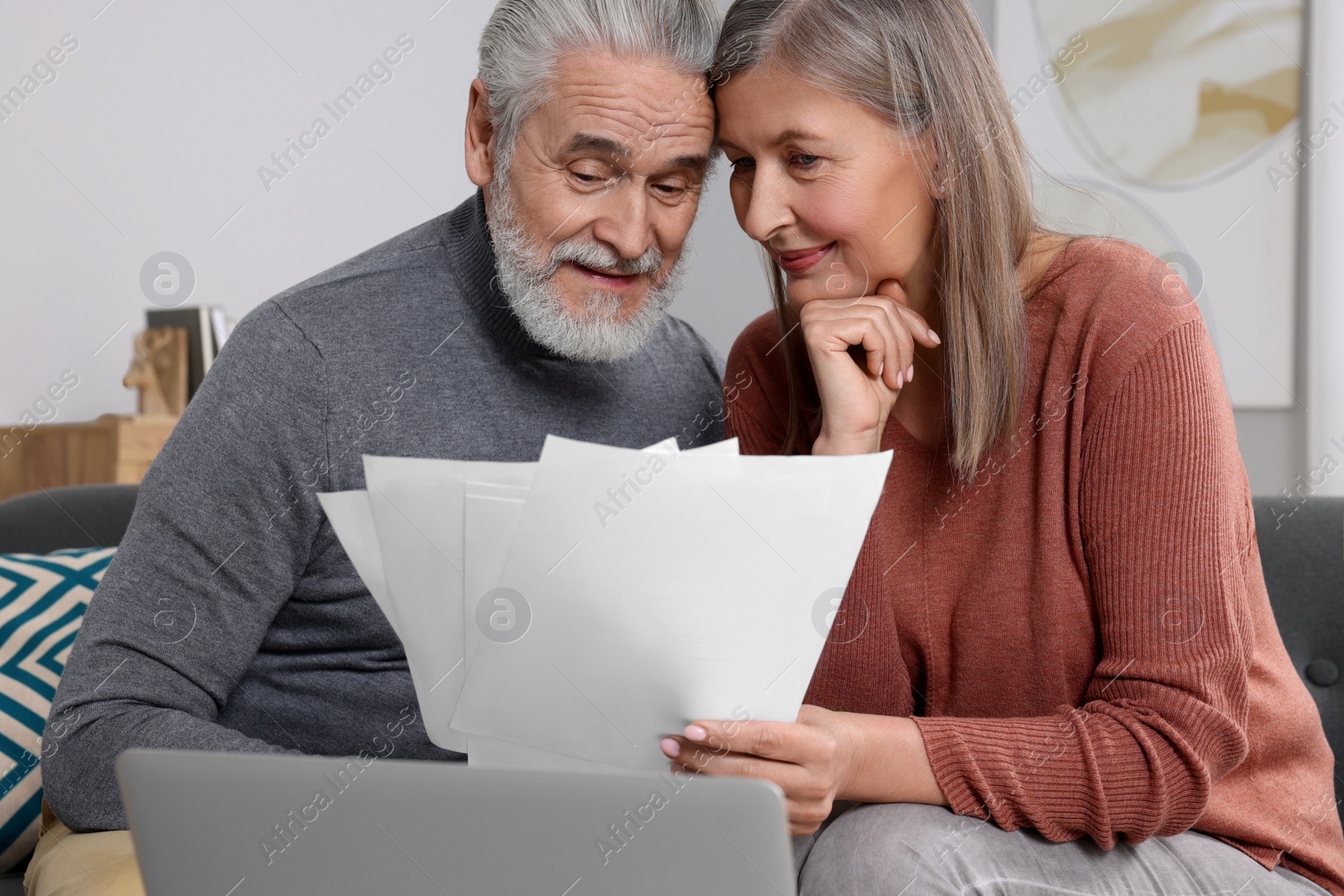 Photo of Elderly couple with papers and laptop discussing pension plan in room