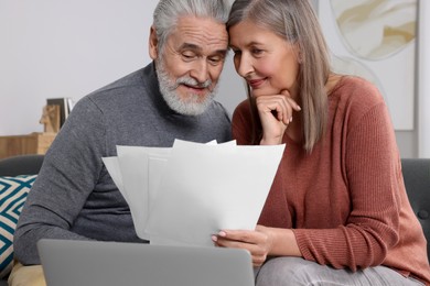 Elderly couple with papers and laptop discussing pension plan in room