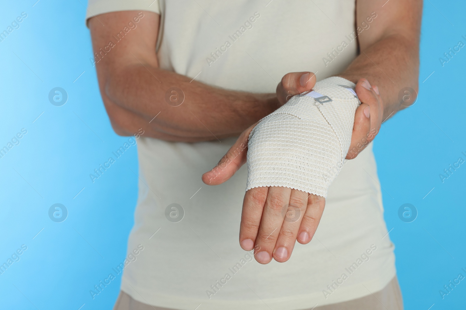 Photo of Man with hand wrapped in medical bandage on light blue background, closeup