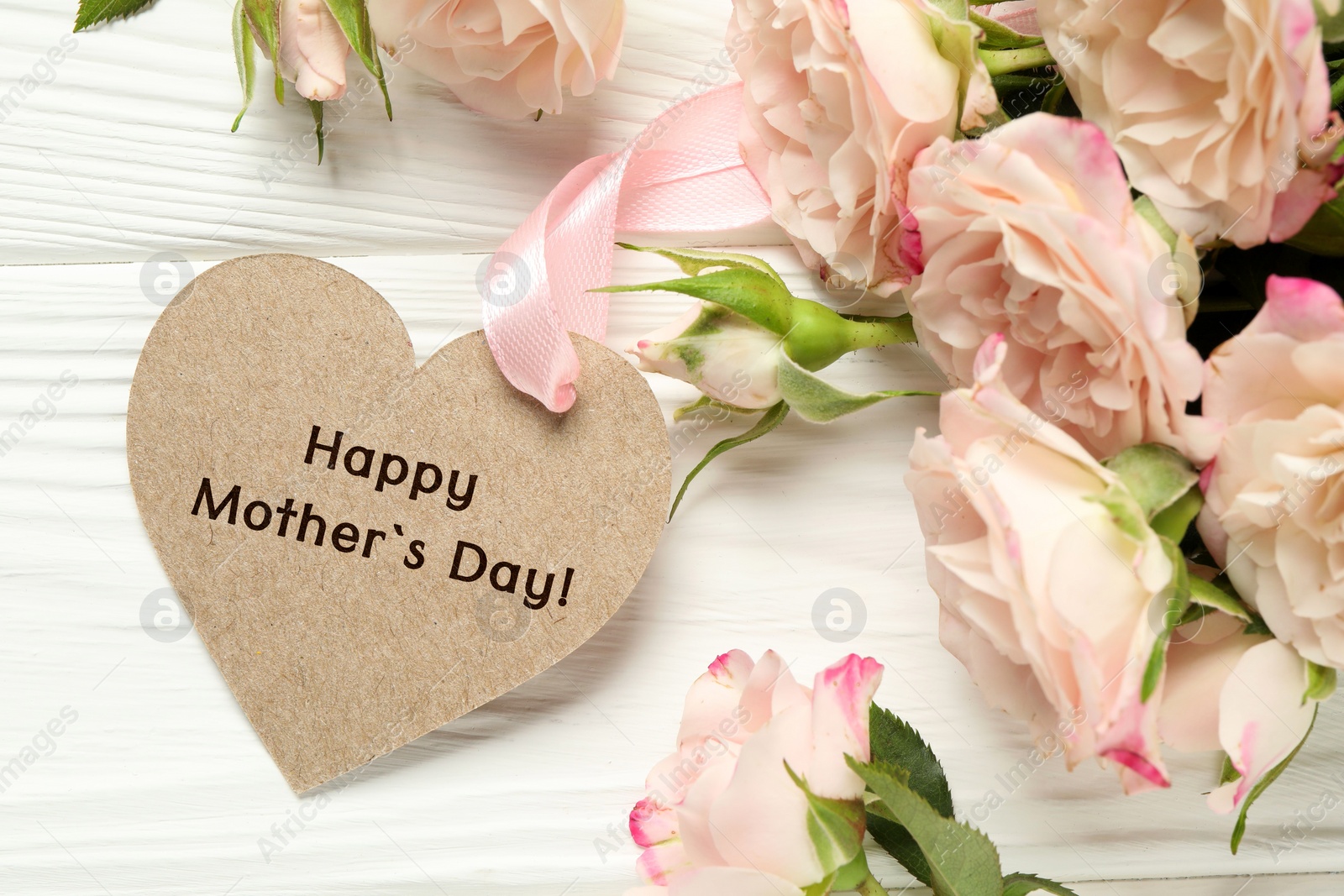 Image of Happy Mother's Day. Heart shaped greeting label and beautiful flowers on white wooden table