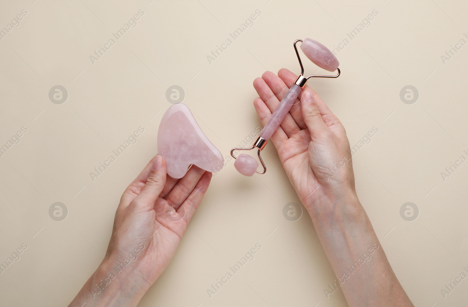 Photo of Woman holding gua sha tool and face roller on beige background, top view