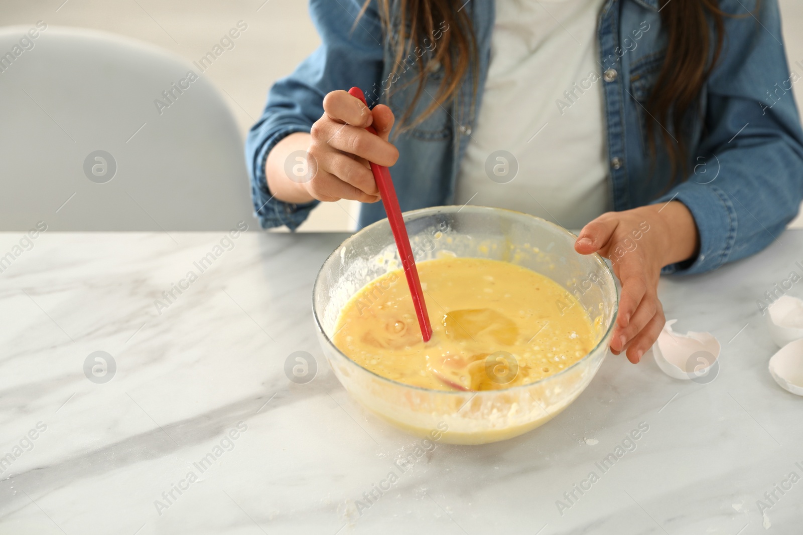 Photo of Cute little girl cooking dough at table in kitchen, closeup