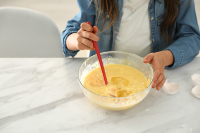 Cute little girl cooking dough at table in kitchen, closeup