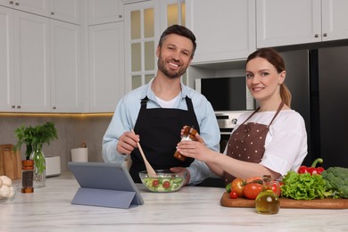 Photo of Happy couple reading recipe on tablet while cooking in kitchen. Online culinary book