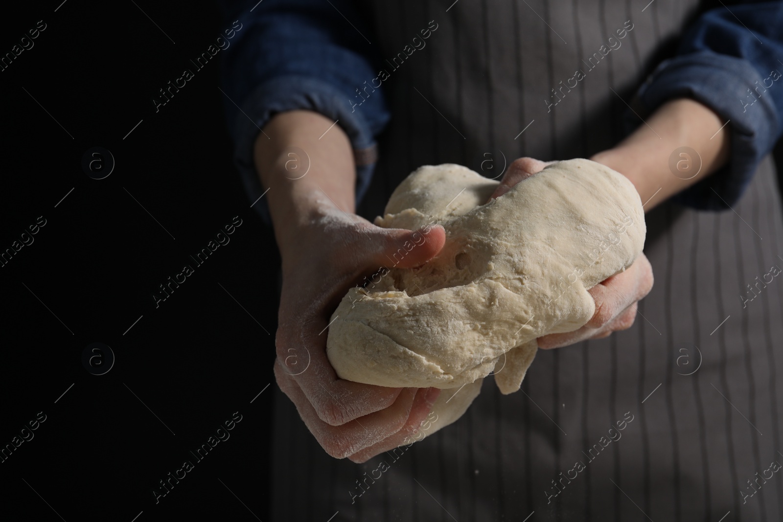 Photo of Making bread. Woman kneading dough on dark background, closeup. Space for text