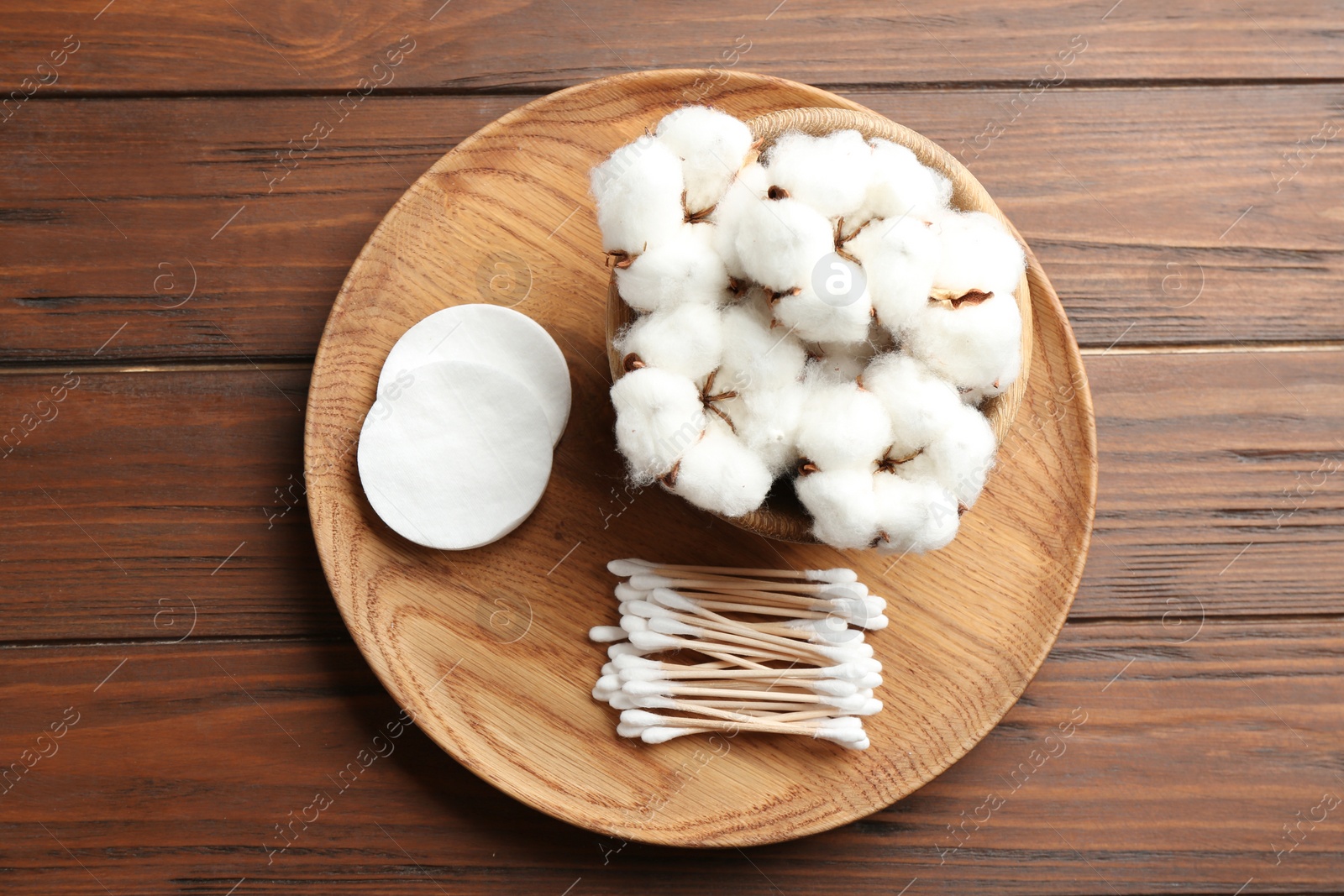 Photo of Plate with cotton swabs, pads and flowers on wooden background, top view