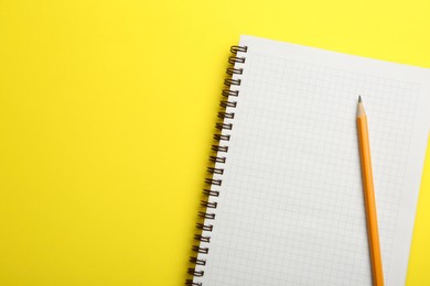 Notebook and pencil on yellow background, top view. Space for text