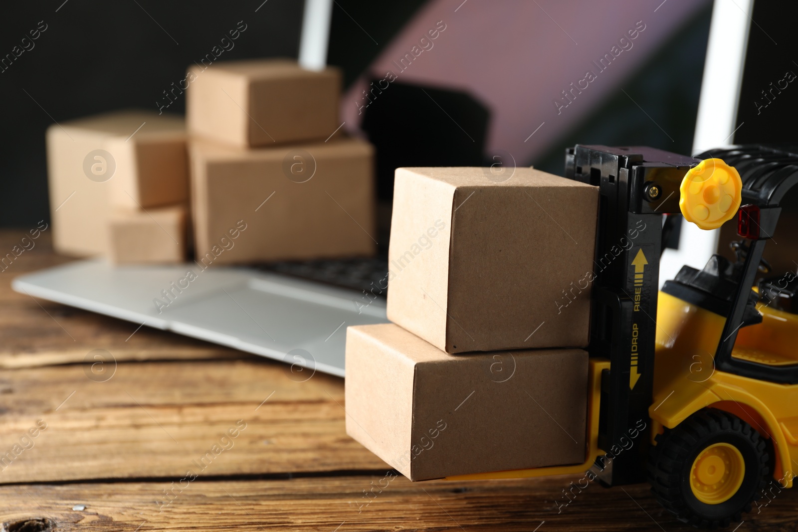 Photo of Toy forklift with boxes near laptop on wooden table. Logistics and wholesale concept