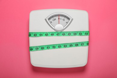 Photo of Bathroom scale tied with measure tape on pink background, top view