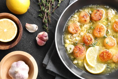 Photo of Delicious scallops with sauce in frying pan and ingredients on dark gray textured table, flat lay
