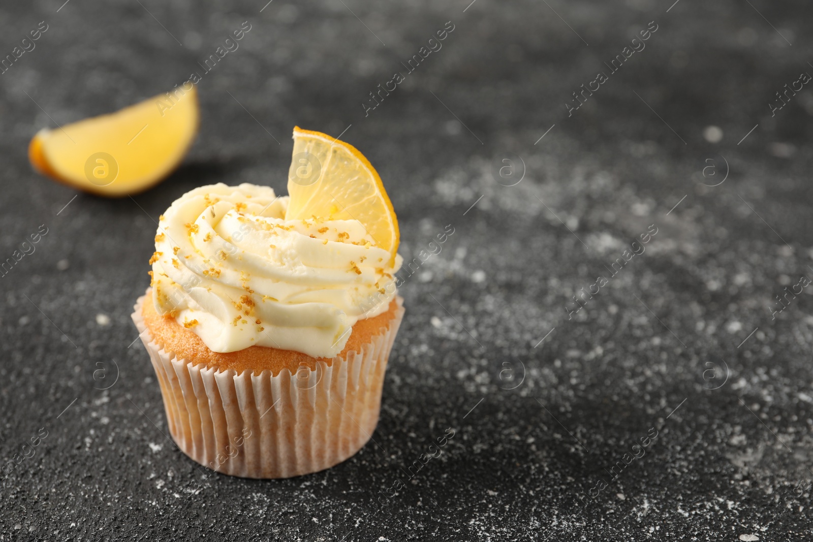 Photo of Tasty cupcake with cream, zest and lemon slice on black textured table, closeup. Space for text