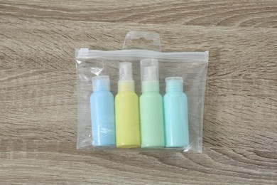 Photo of Cosmetic travel kit in plastic bag on wooden table, top view. Bath accessories