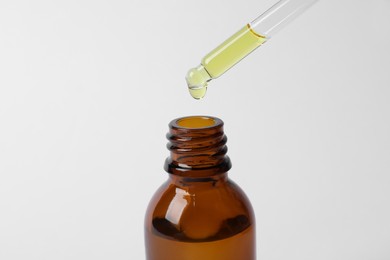 Photo of Dripping cosmetic oil from pipette into bottle on white background, closeup