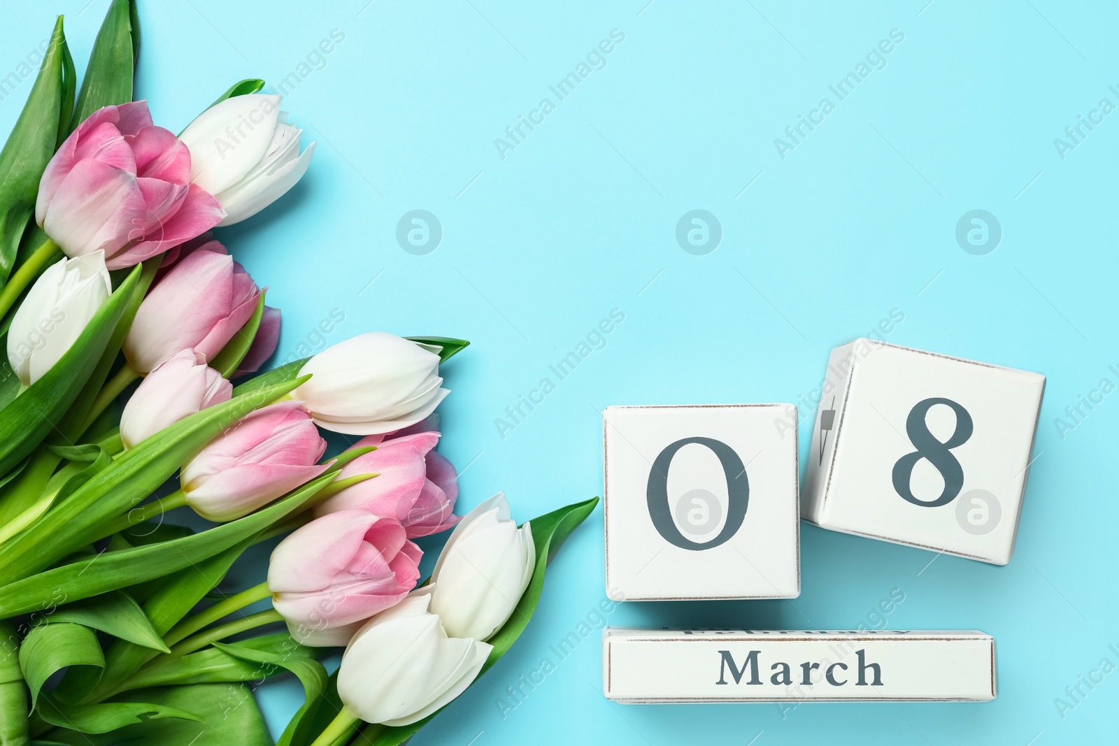 Photo of Wooden block calendar with date 8th of March and tulips on light blue background, flat lay. Space for text