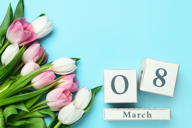 Photo of Wooden block calendar with date 8th of March and tulips on light blue background, flat lay. Space for text