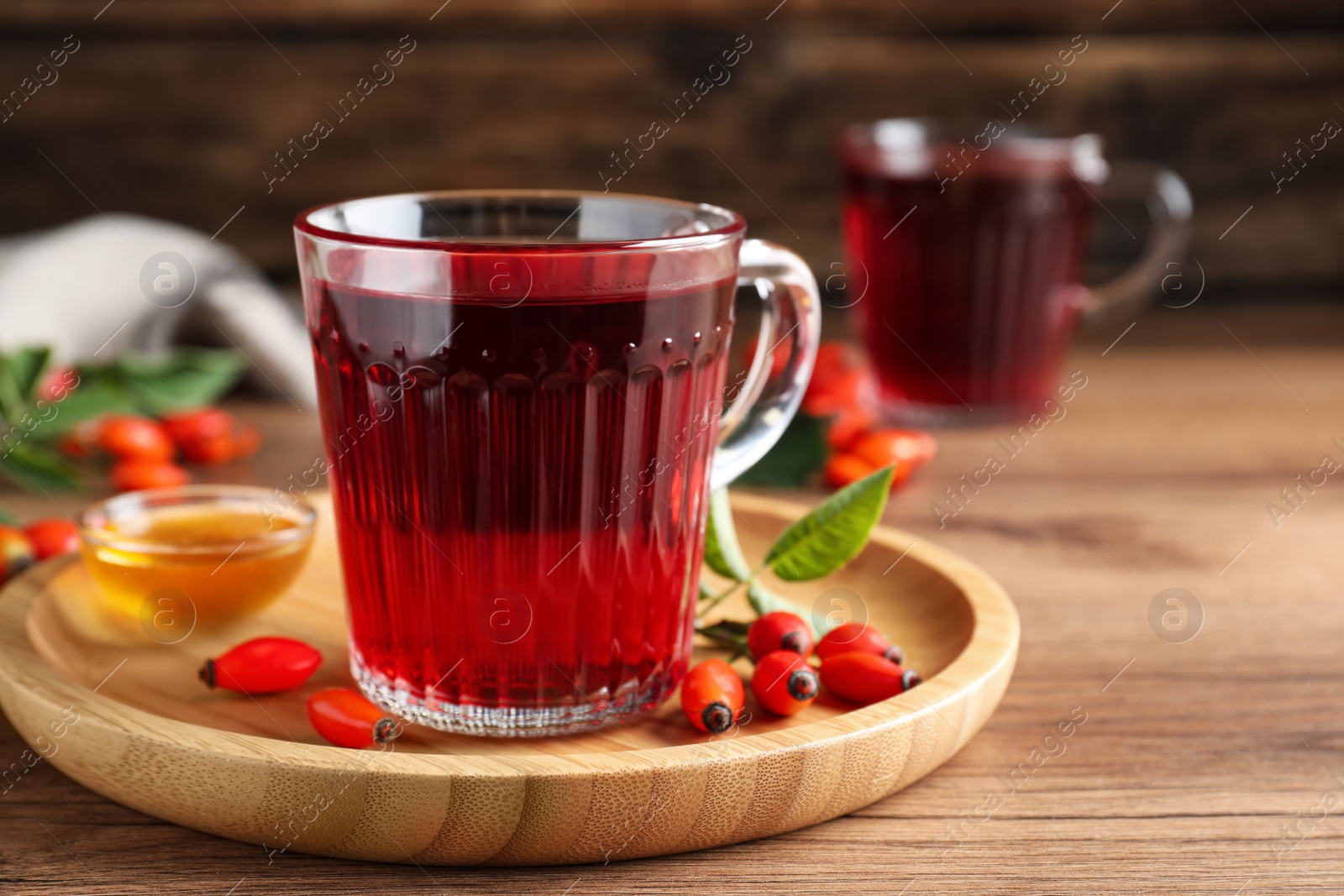 Photo of Fresh rose hip tea, honey and berries on wooden table