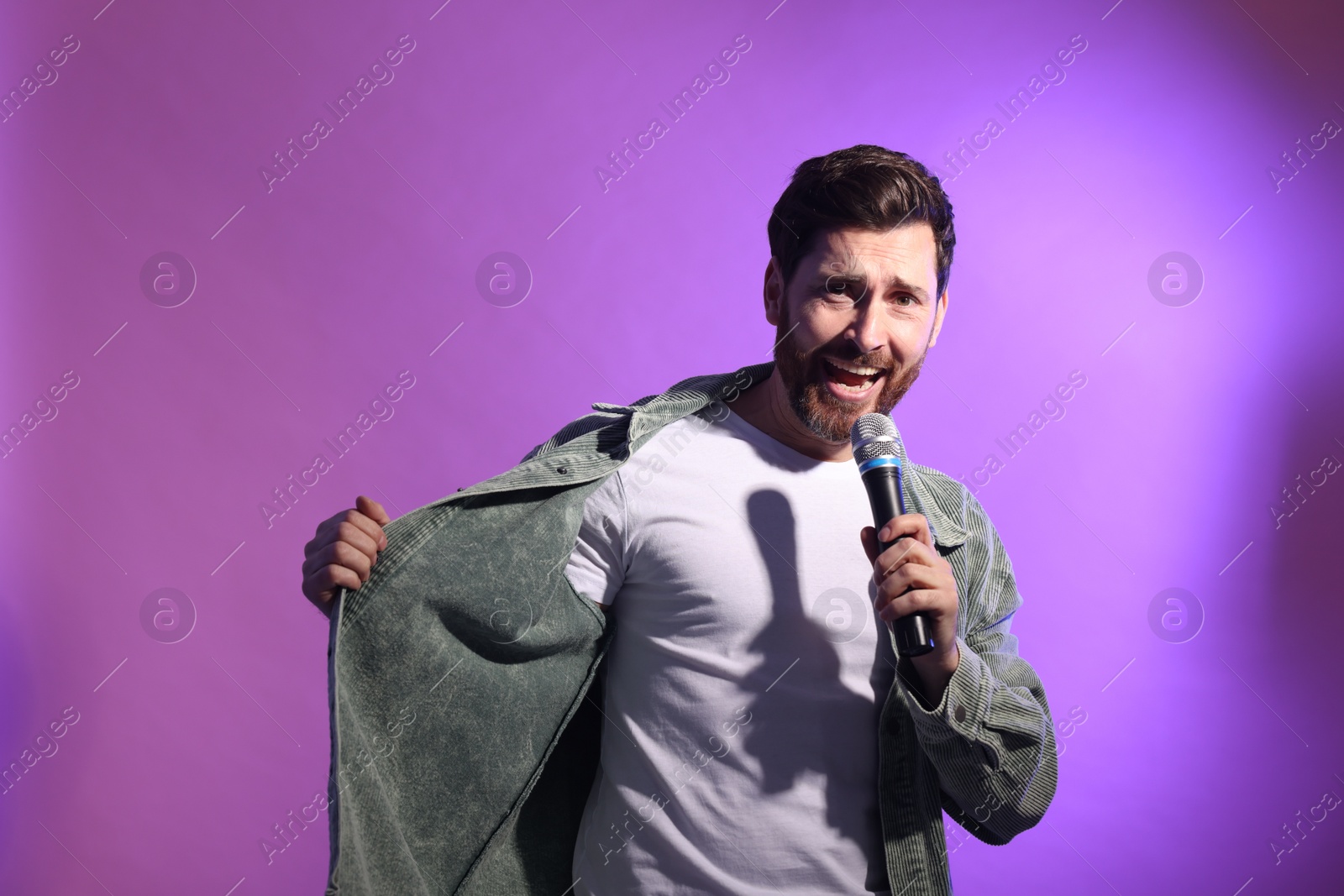 Photo of Handsome man with microphone singing on violet background