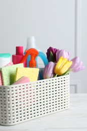 Photo of Spring cleaning. Basket with detergents, flowers and tools on white wooden table