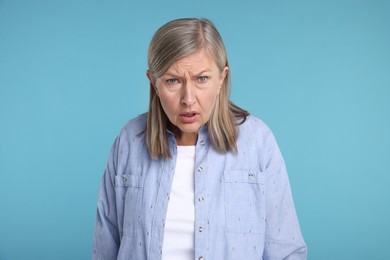 Portrait of surprised senior woman on light blue background