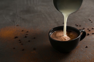Photo of Pouring milk into cup with tasty hot chocolate on table. Space for text