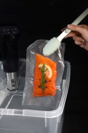Photo of Woman putting vacuum packed salmon into box with thermal immersion circulator, closeup. Sous vide cooking