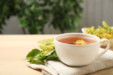 Cup of tea with linden blossom on wooden table. Space for text