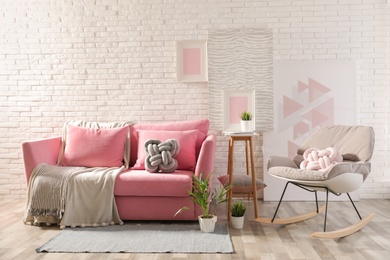 Stylish living room interior with sofa and rocking armchair near brick wall