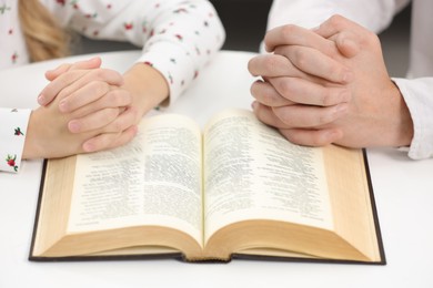 Photo of Girl and her godparent praying over Bible together at table indoors, closeup