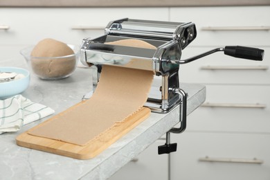 Photo of Preparing dough for soba (buckwheat noodles) with pasta maker at light grey table in kitchen