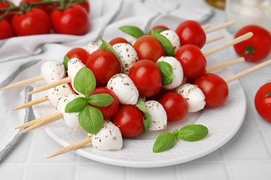 Photo of Caprese skewers with tomatoes, mozzarella balls, basil and spices on white table, closeup