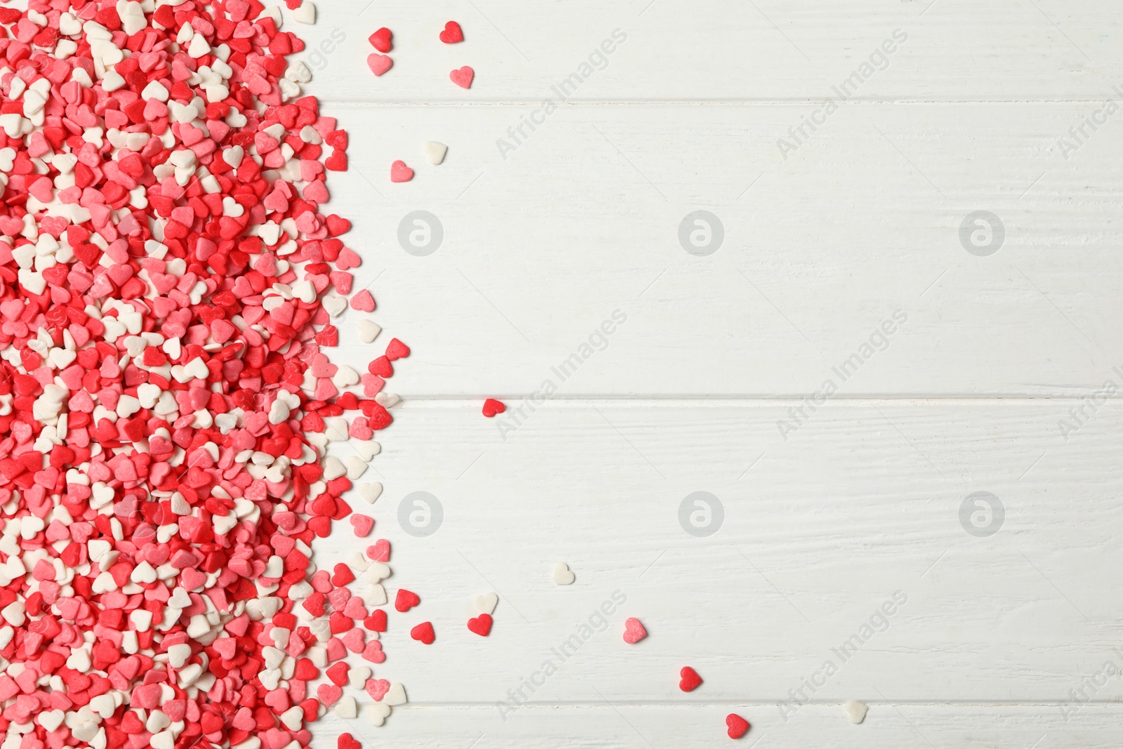 Photo of Bright heart shaped sprinkles on white wooden table, flat lay. Space for text