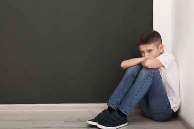 Photo of Upset boy sitting on floor indoors. Space for text